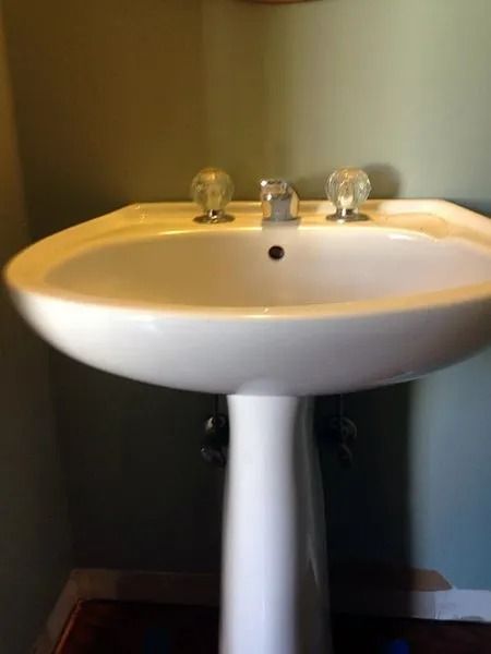 White pedestal sink with clear glass knobs on a light green wall.