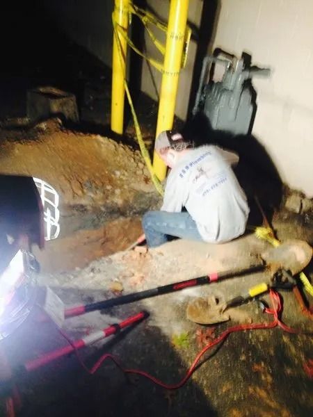 Workers excavating near yellow poles at night. A man kneels, tools and wires nearby.