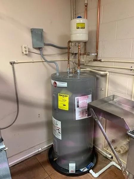 A water heater in a corner, with copper pipes and a white expansion tank.