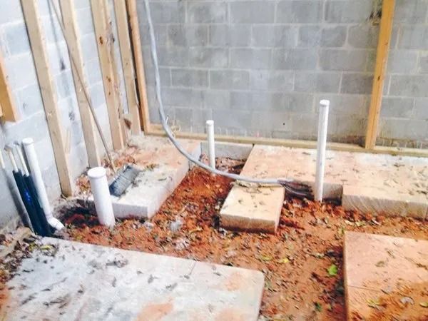 Bathroom remodel in progress with exposed pipes and concrete blocks on dirt floor.