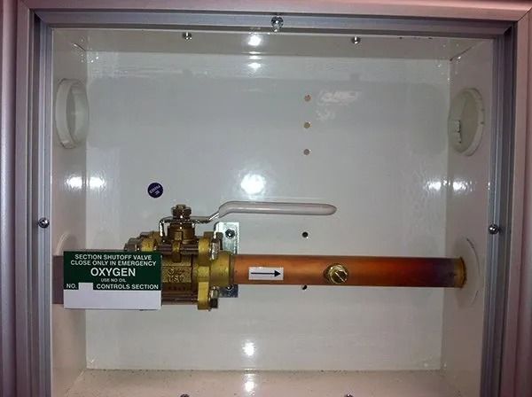 Oxygen valve assembly inside a white cabinet, with copper piping and a green label.