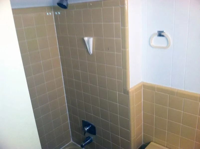 Tan tiled shower and adjacent wall with white paneling and a towel ring.