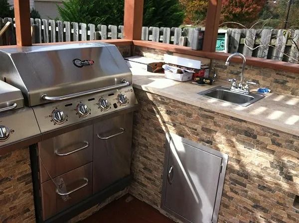 Outdoor kitchen with stainless steel grill, sink, and stone facade.