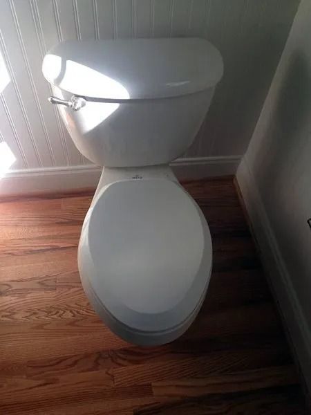 White toilet in a bathroom, viewed from above, with wooden floors and white paneling on the wall.