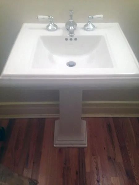 White pedestal sink with chrome fixtures, set against a wooden floor.