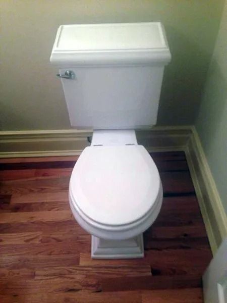 White toilet on wooden floor in a bathroom, viewed from above.