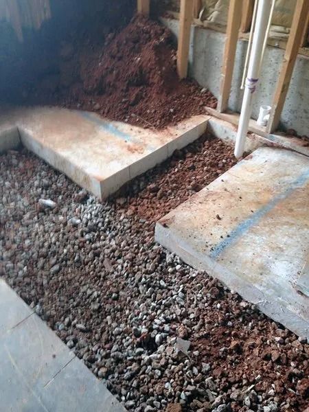 Construction site: Concrete pads, gravel, and dirt fill space between wooden framing.