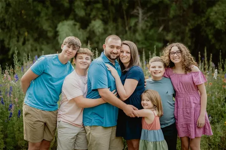 Family of seven, smiling and embracing in a garden, wearing colorful summer clothes.