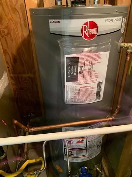 Rheem water heater in a utility closet with exposed pipes and wooden framing
