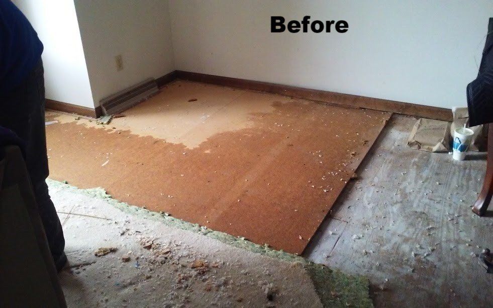 A room with exposed flooring and remnants of carpet;