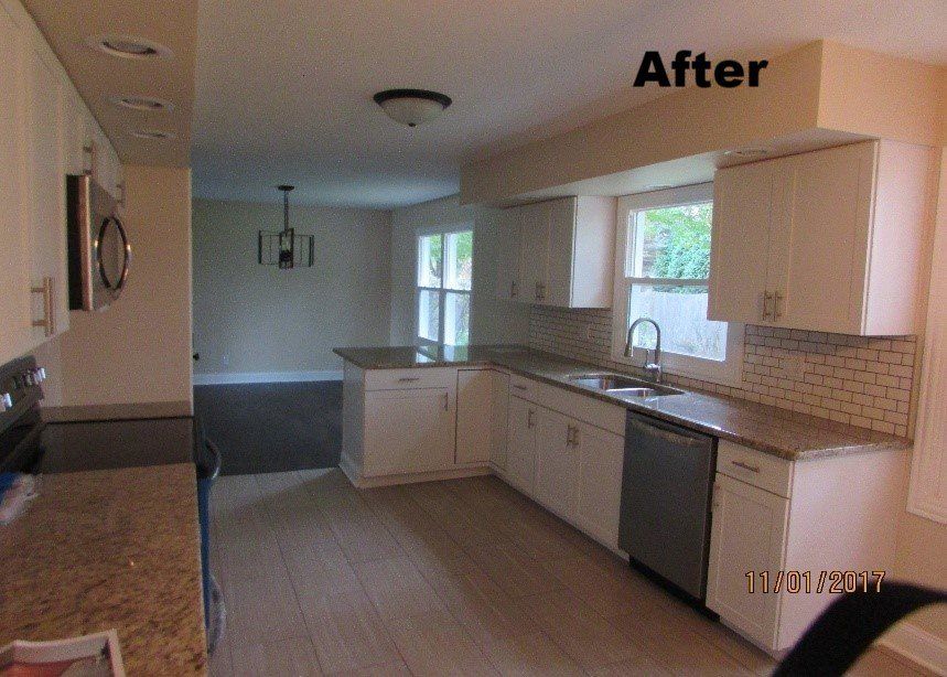 Remodeled kitchen with white cabinets, granite countertops, and light wood flooring.  The space includes stainless steel appliances and a view into another room.