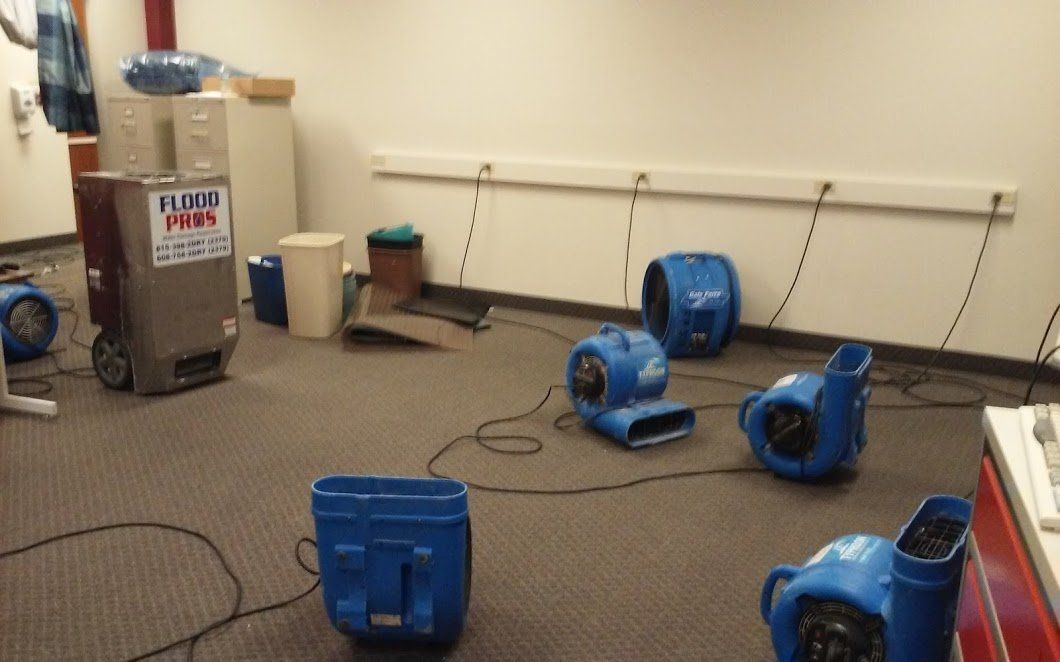 Several blue fans and a dehumidifier are drying a carpeted room.