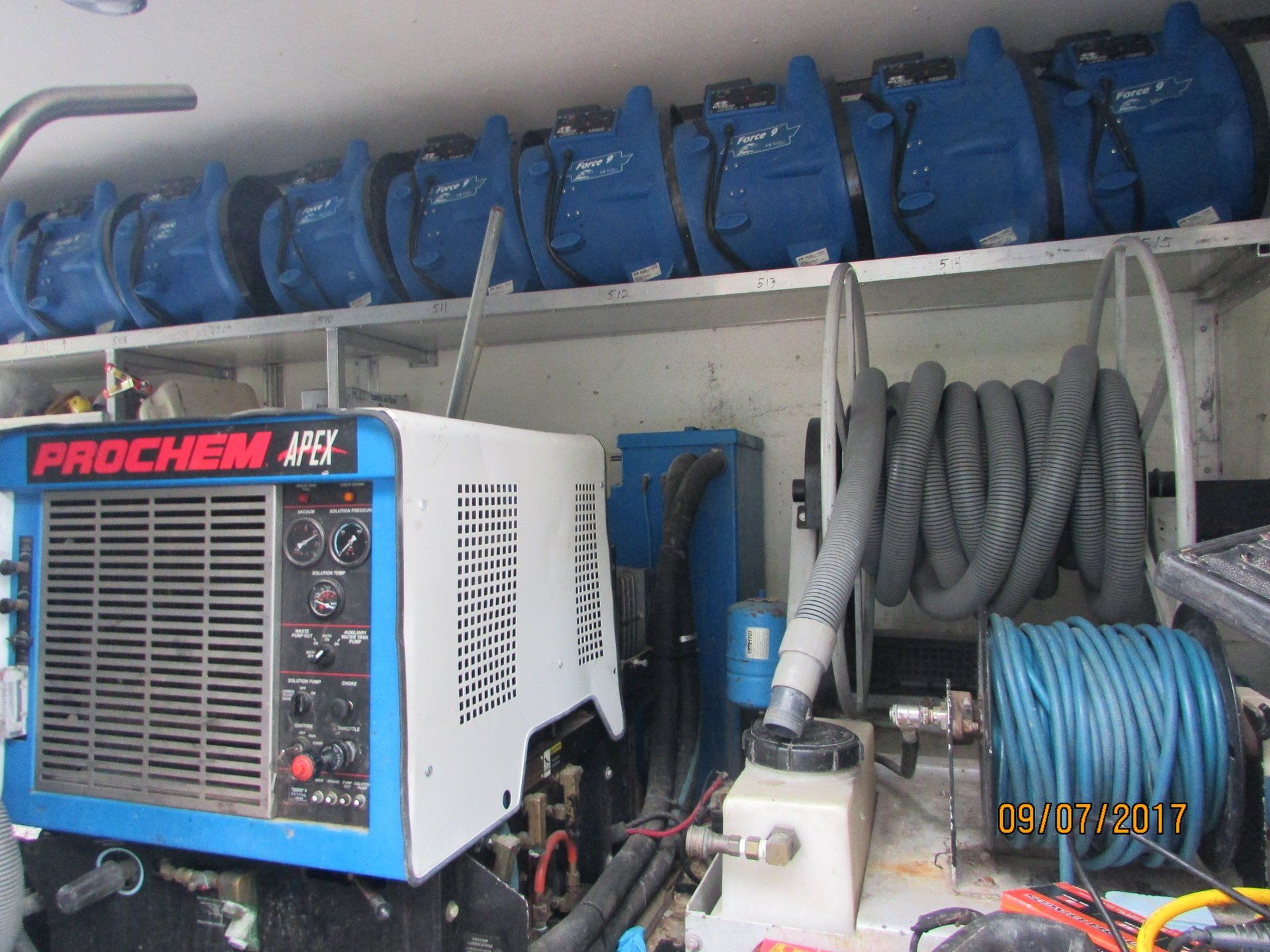 Inside a truck: a carpet cleaning machine, hoses, and blue air movers on a shelf.