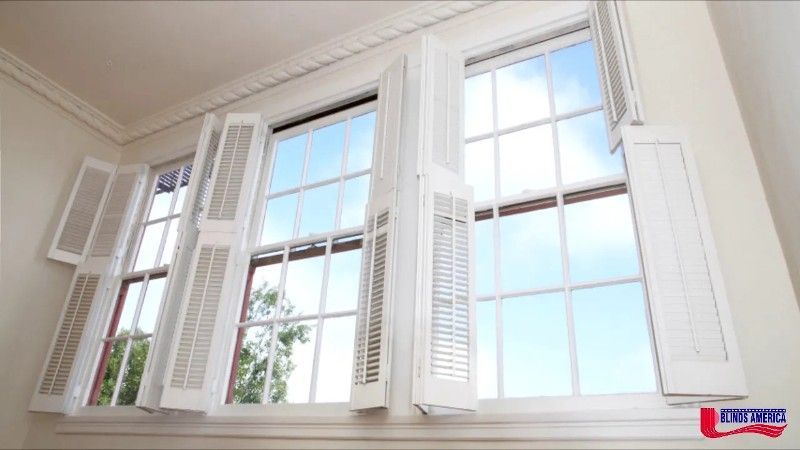 A window with white shutters is open to a blue sky