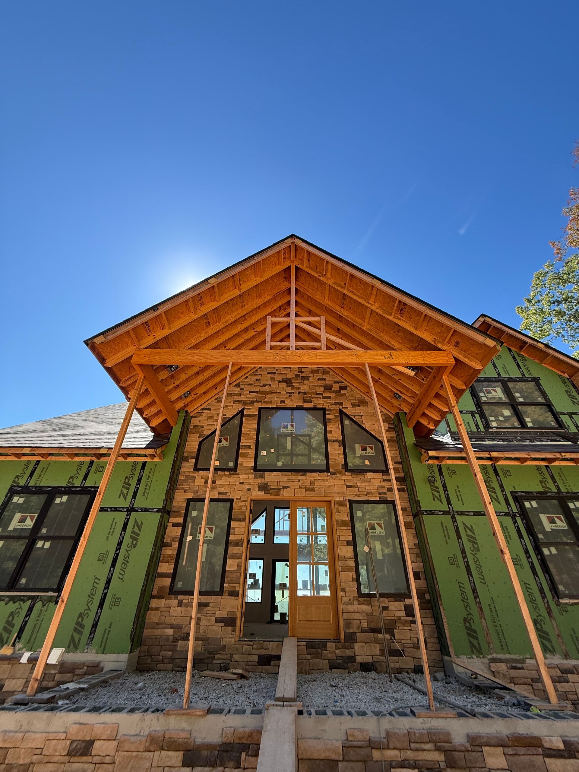 Rustic lodge entrance with timber roof, stone facade, and green window shutters under a clear blue sky