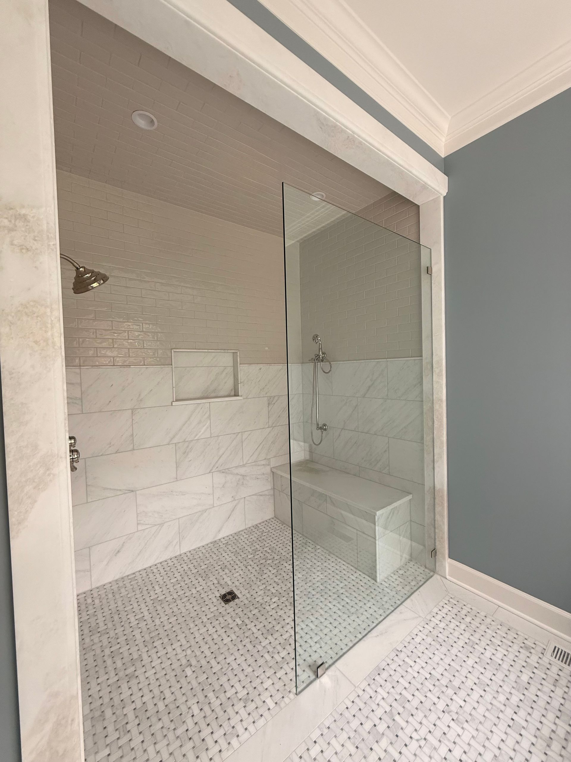 Modern shower with glass door, marble tile walls, and pebble mosaic floor in a bathroom