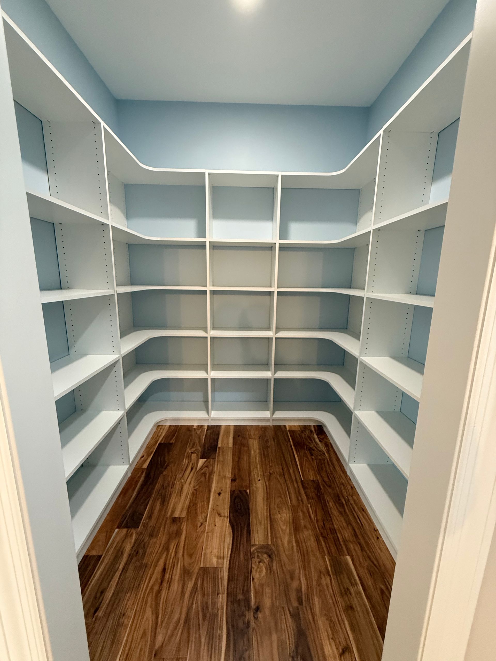Empty walk-in closet with white shelving and brown wood floor.