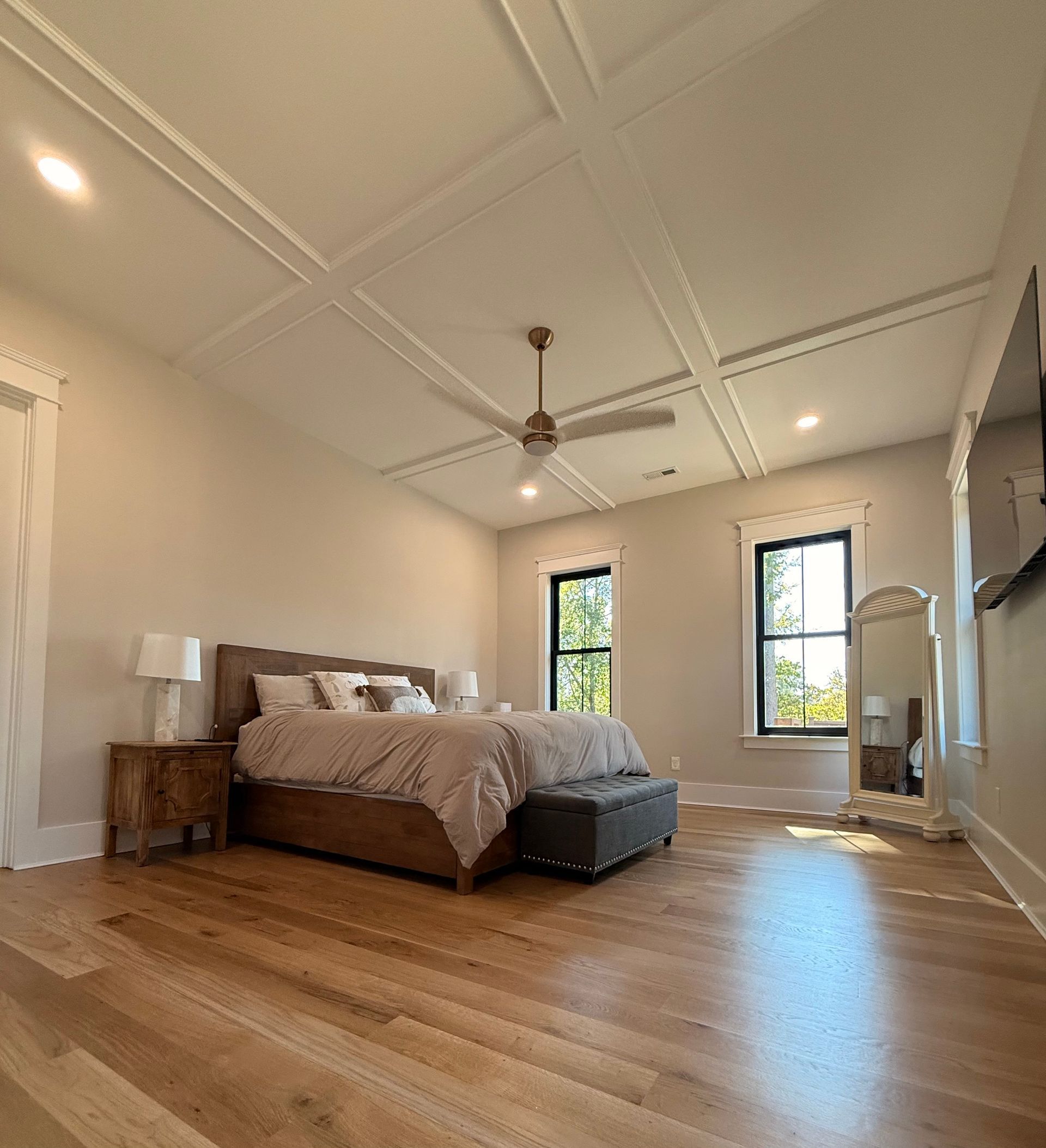 Bright bedroom with hardwood floors, white coffered ceiling, bed, and two tall windows.
