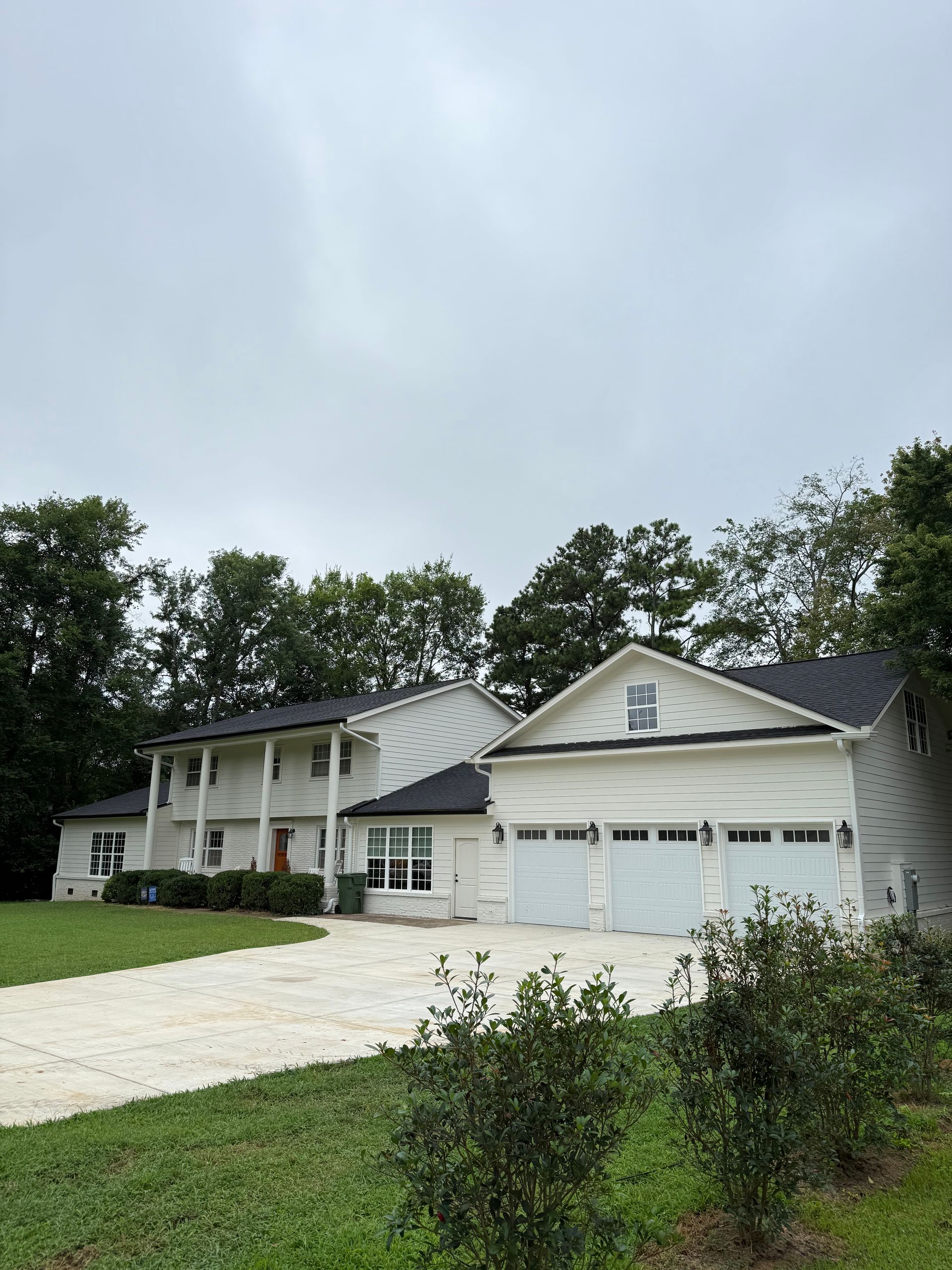 Suburban two-story white house with attached garage, driveway, and trees under a cloudy sky