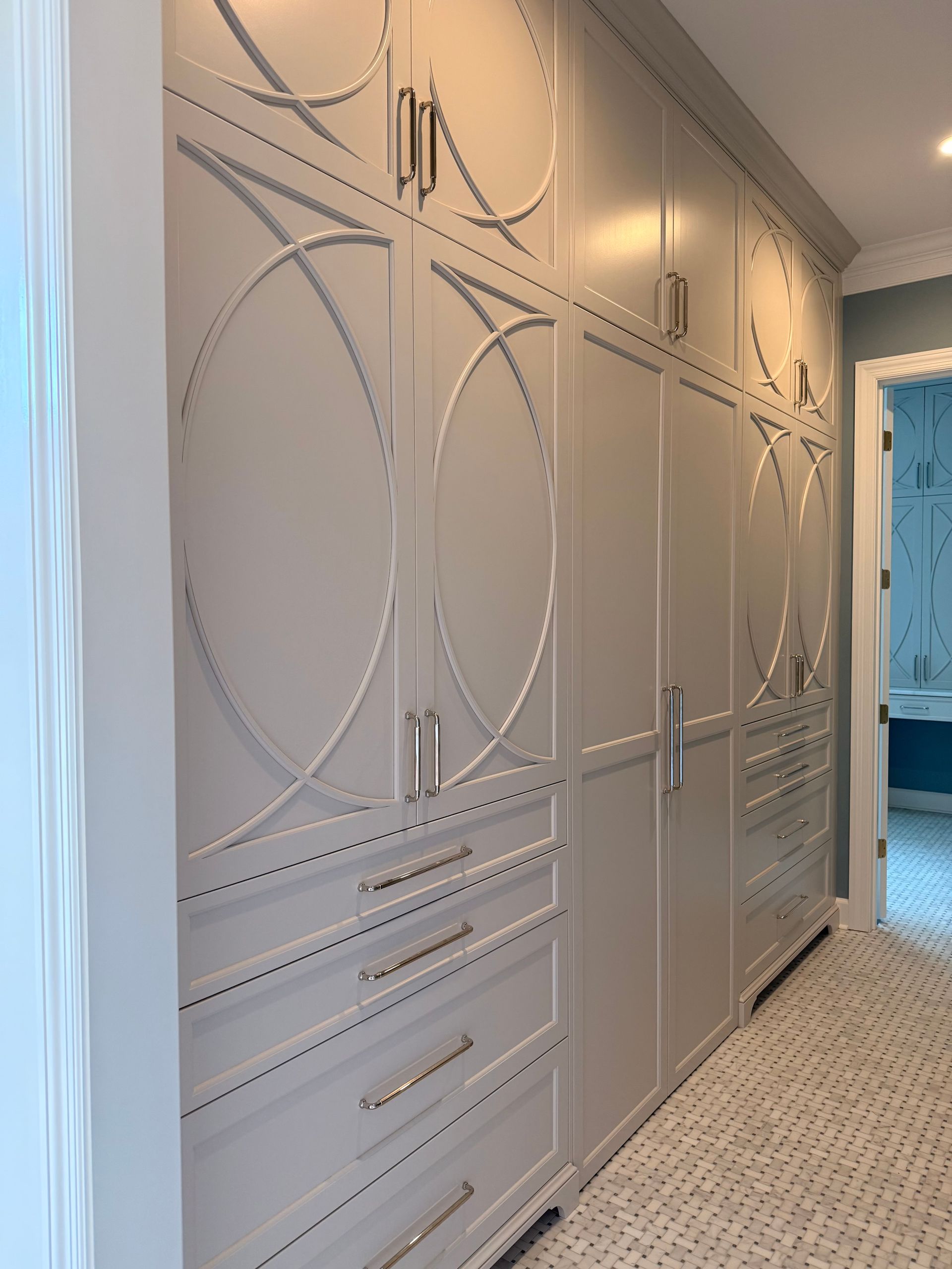 Built-in gray wardrobe with gold hardware along a hallway beside a patterned carpet runner