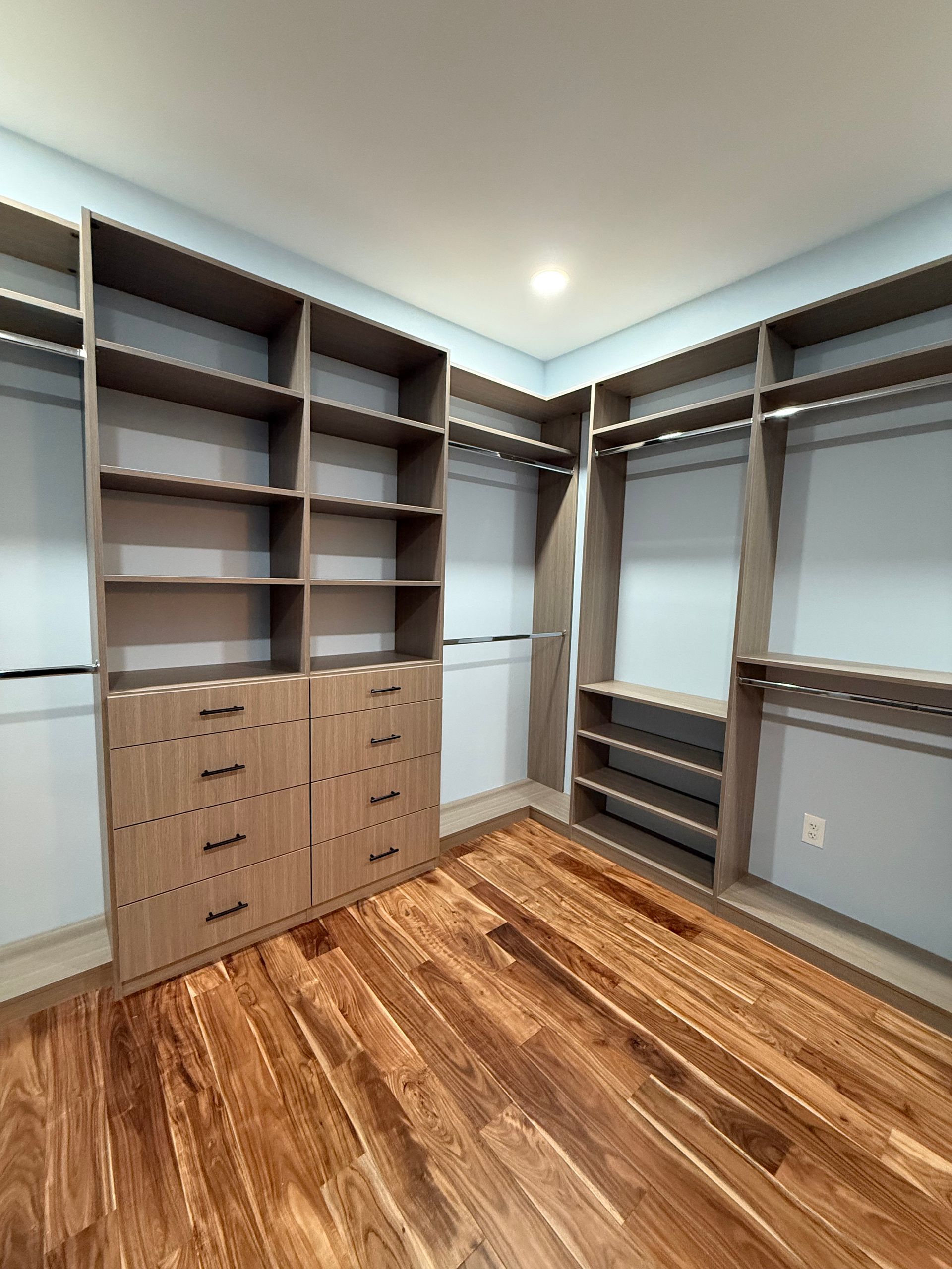 Empty walk-in closet with wood floor, gray built-in shelves, and cabinet drawers around the walls.