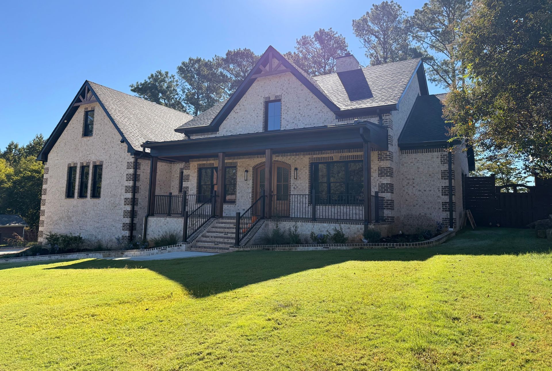 Stone house with a front porch and steep roof, set on a sunny lawn with trees behind it