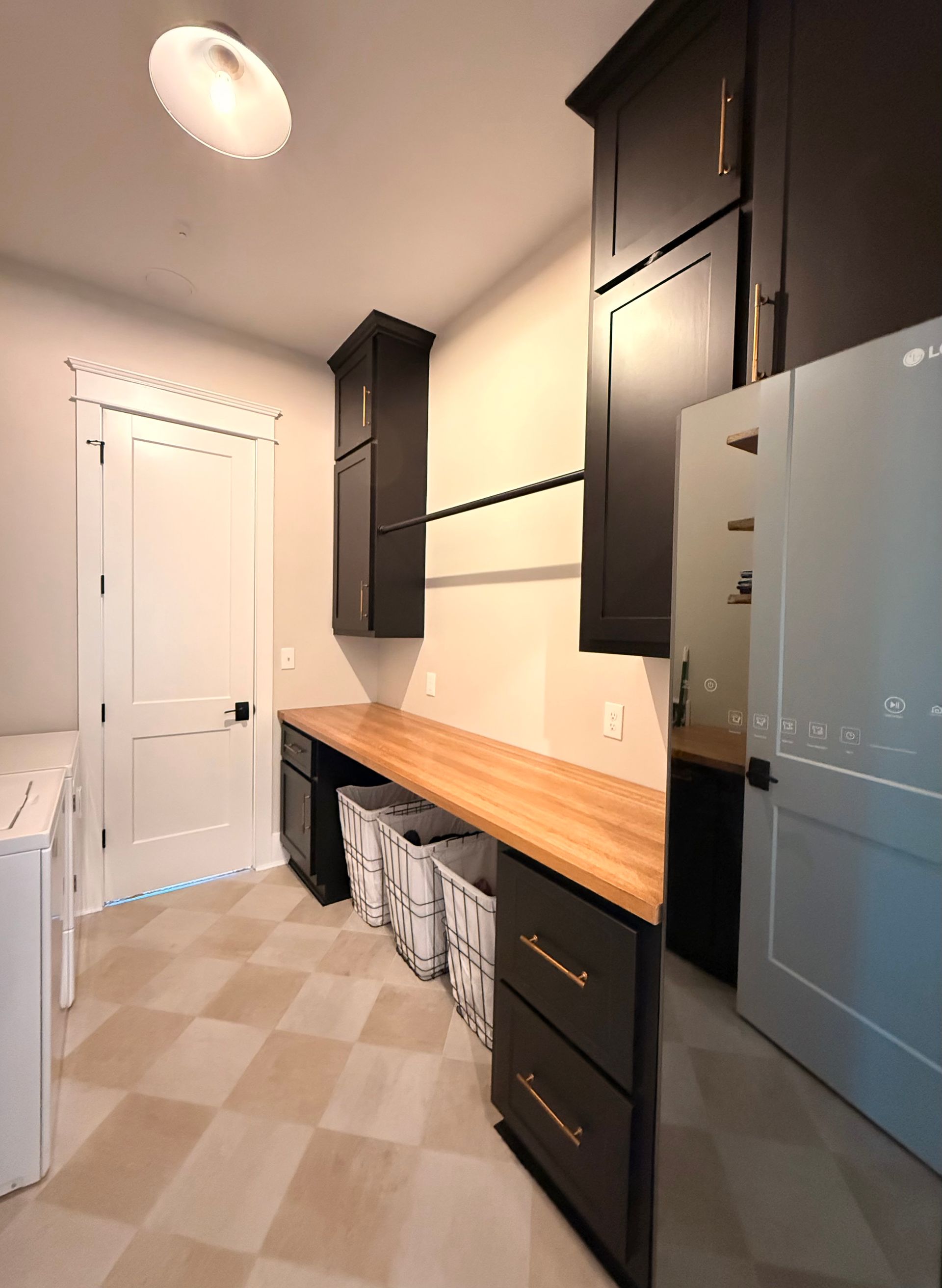 Narrow kitchen with dark cabinets, butcher-block counter, beige tile floor, and white door.