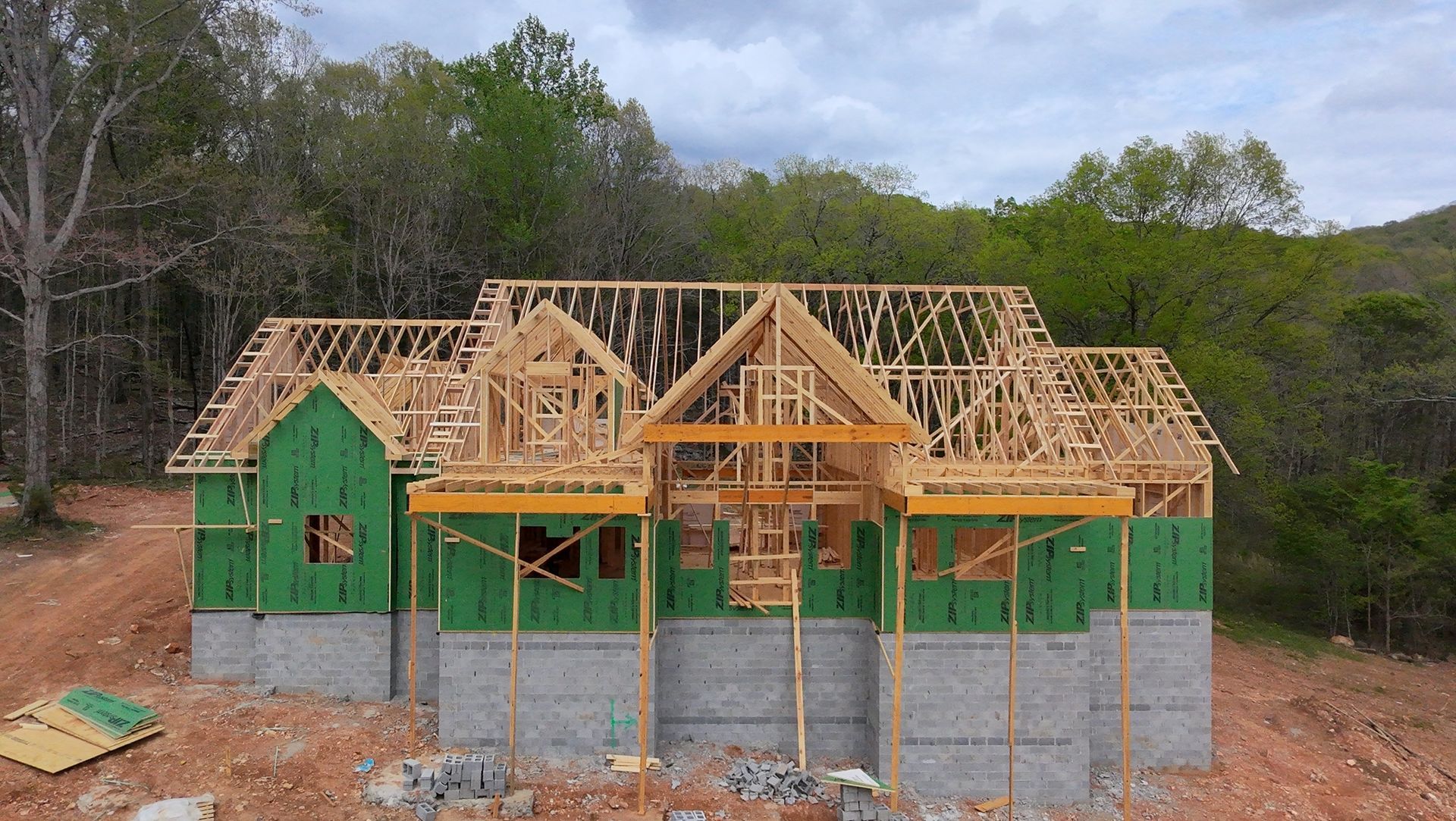 Partially framed green house under construction with exposed roof trusses and concrete block foundation.