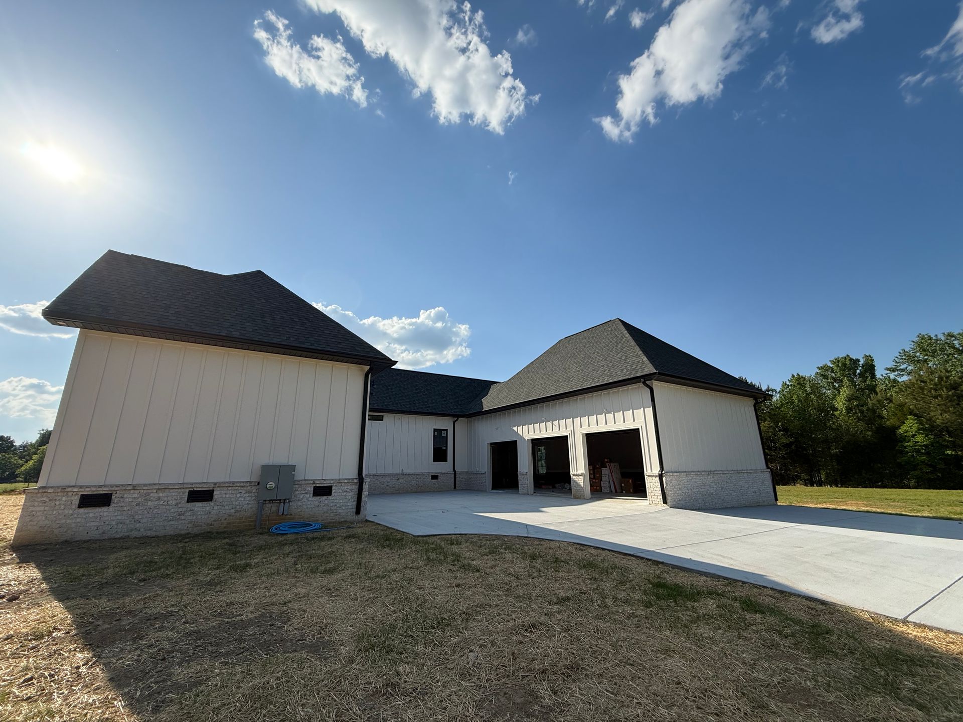New white house under construction with dark roof and concrete driveway under a sunny blue sky