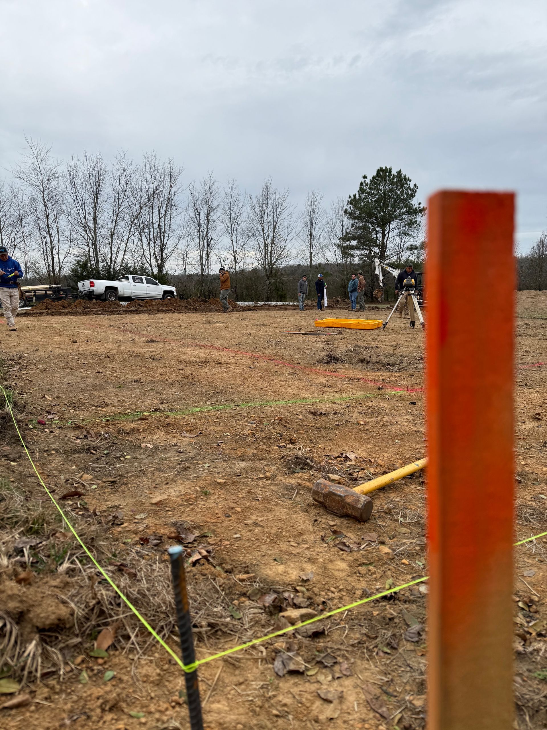 Construction site with an orange stake, yellow string, dirt, and workers in the background.