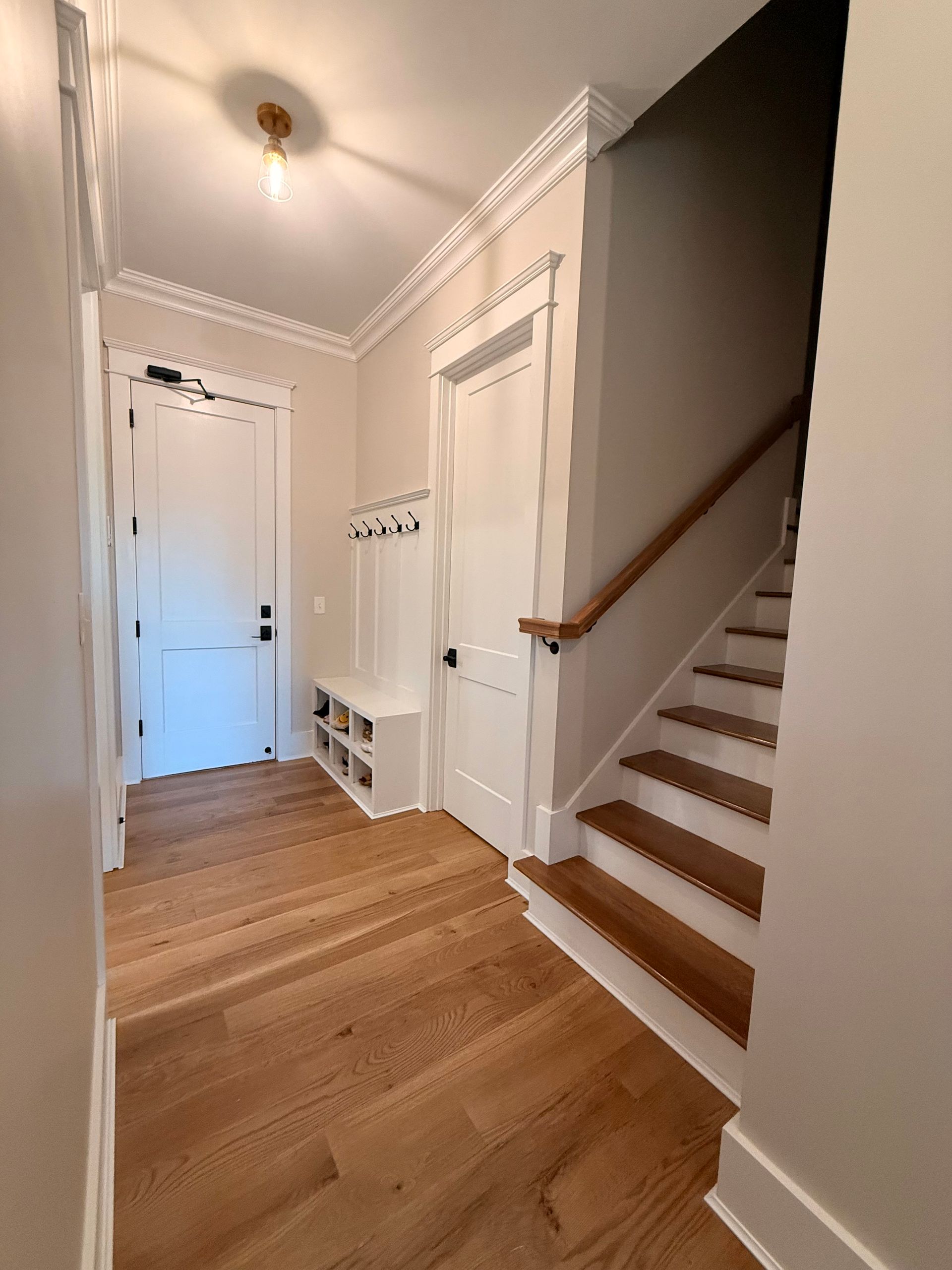 Narrow hallway with hardwood floors, white walls, and a wooden staircase on the right.