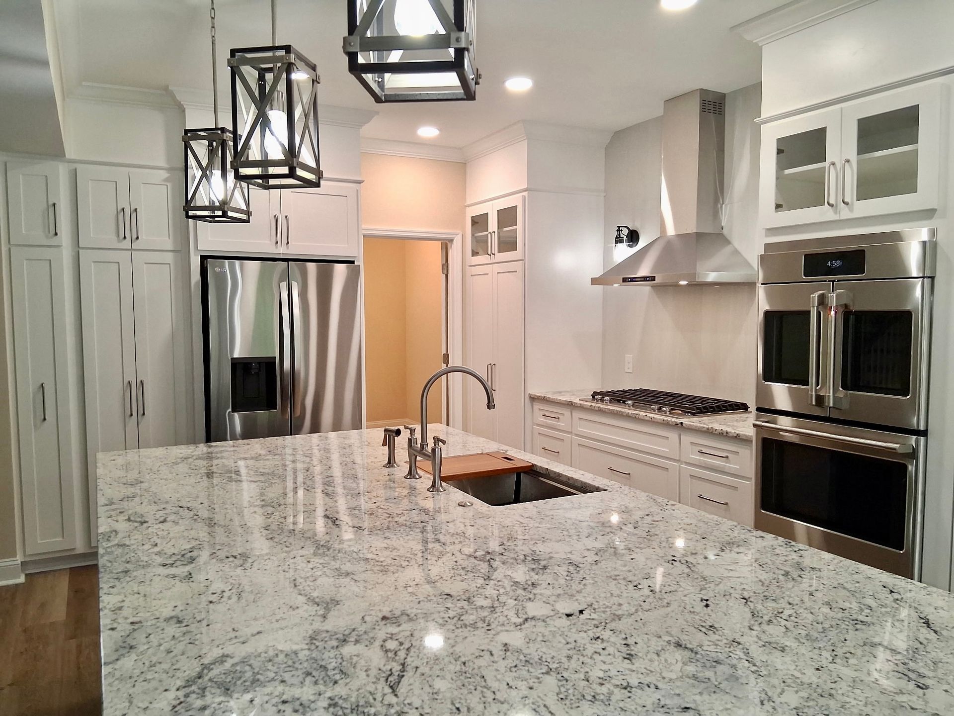 Bright modern kitchen with marble island, stainless appliances, white cabinets, and pendant lights