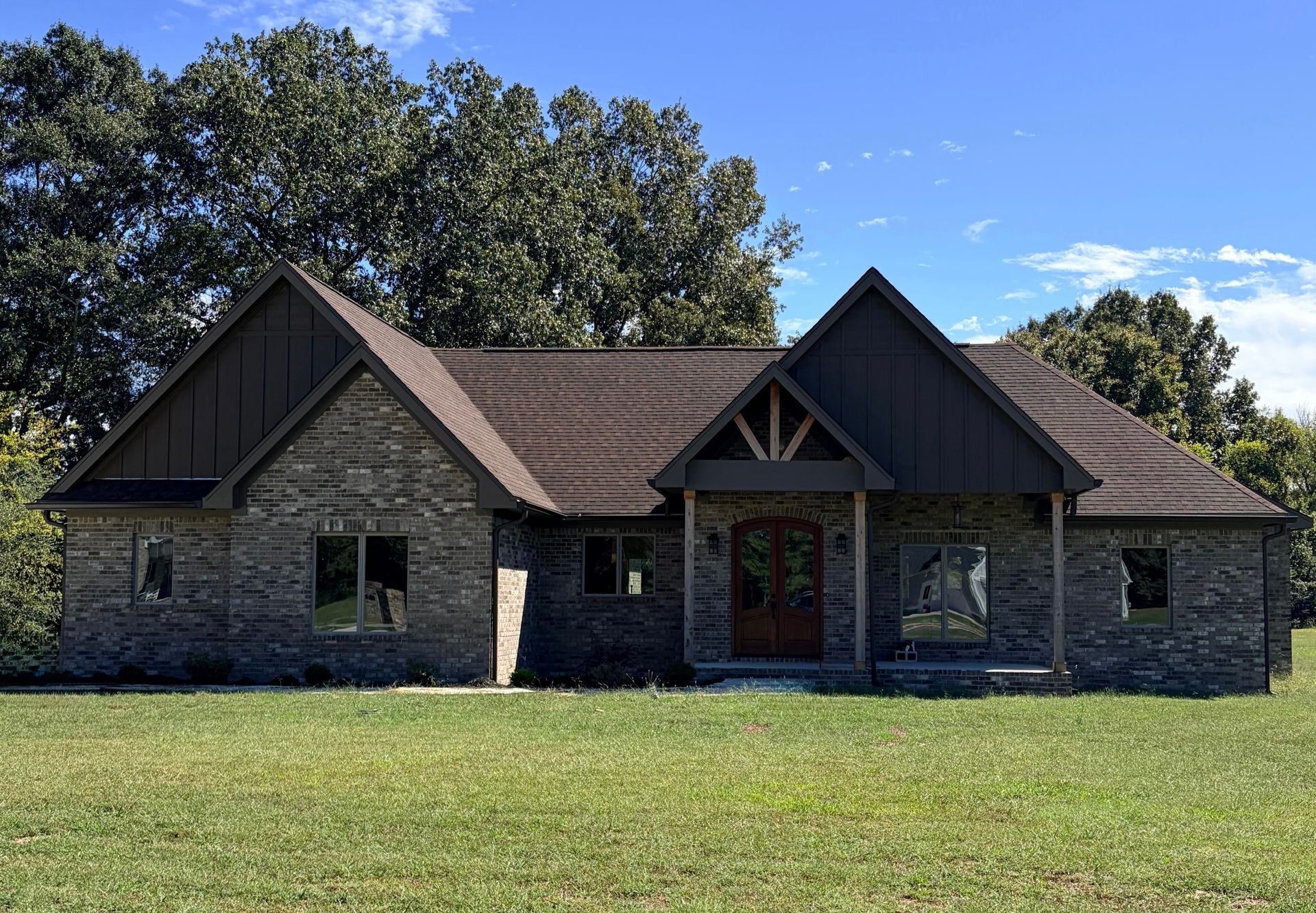 Single-story stone house with brown roof and front porch on a grassy lawn under a blue sky