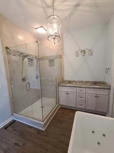 Bathroom with a glass shower, double vanity, bathtub, and wood-look flooring.