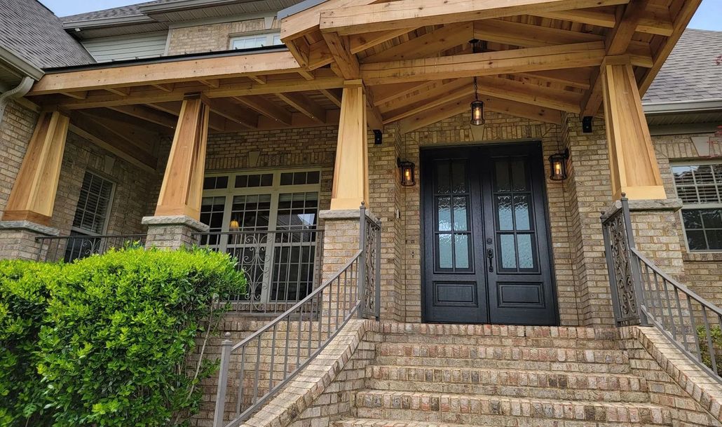 Brick house entrance with porch, double black doors, stone steps, and landscaping.