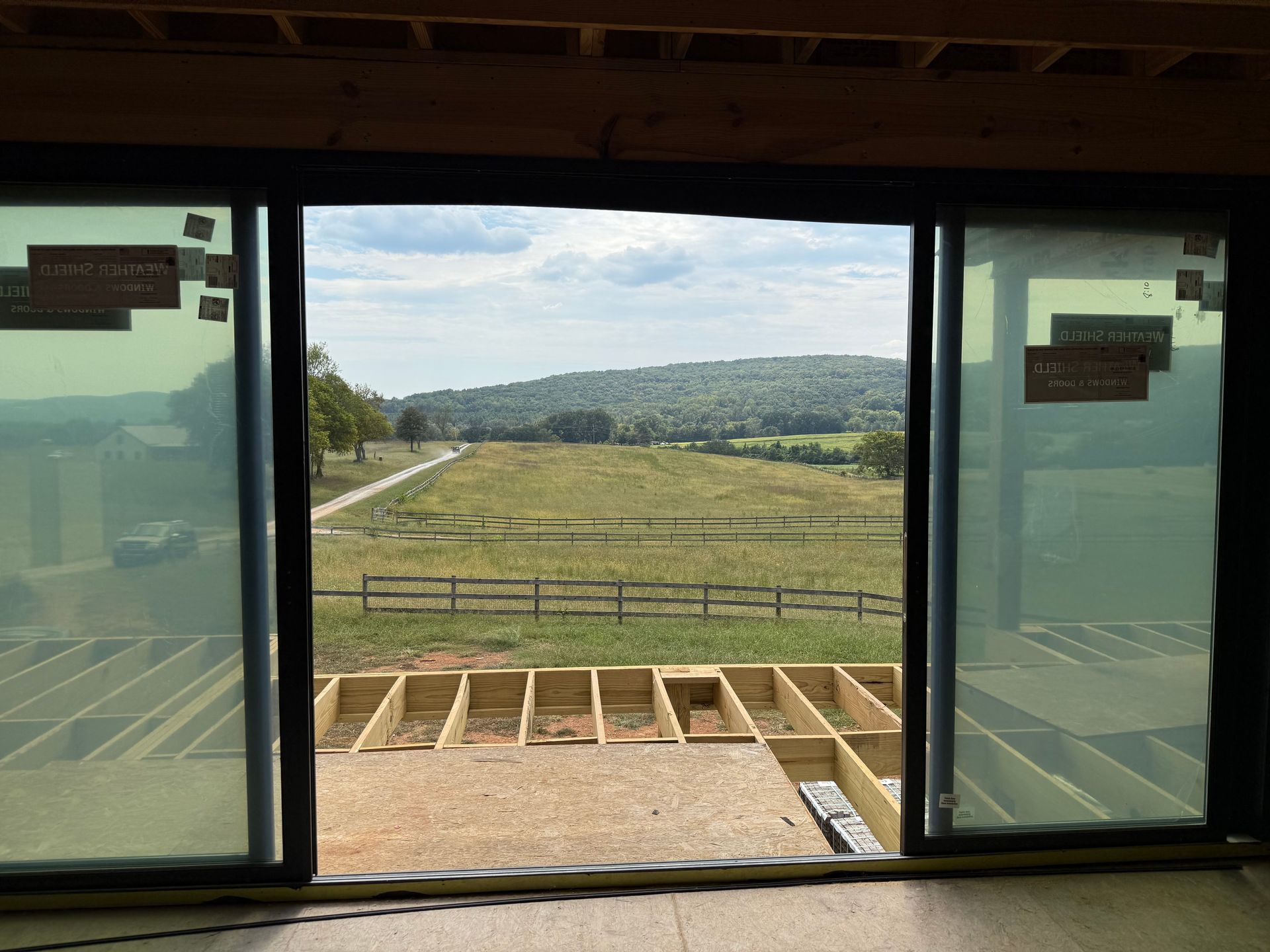 Open sliding glass doors offering a scenic view of a green field, a fence, and distant hills.