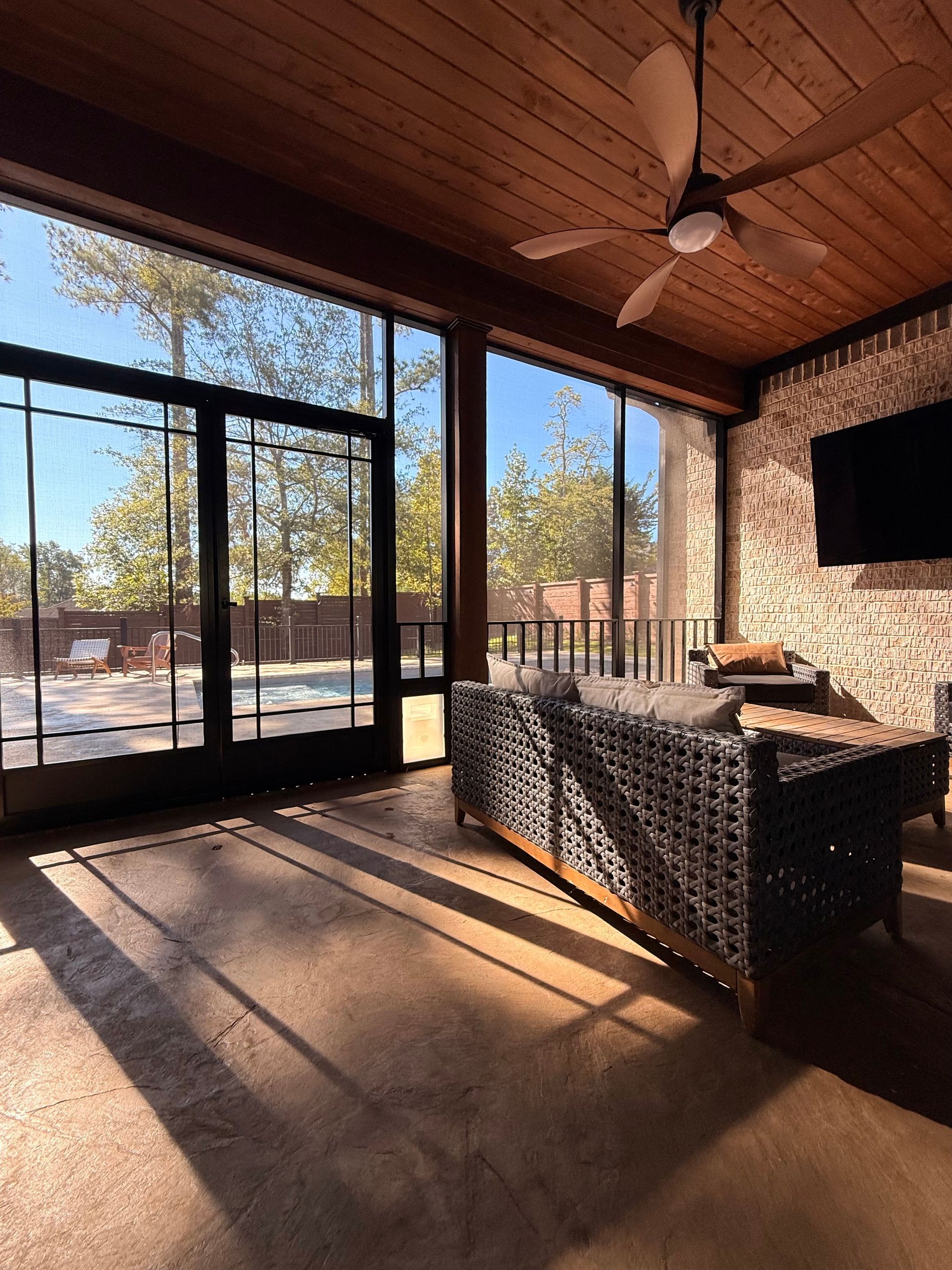 Covered patio with sliding glass doors, wicker seating, and sunlight streaming onto the floor.