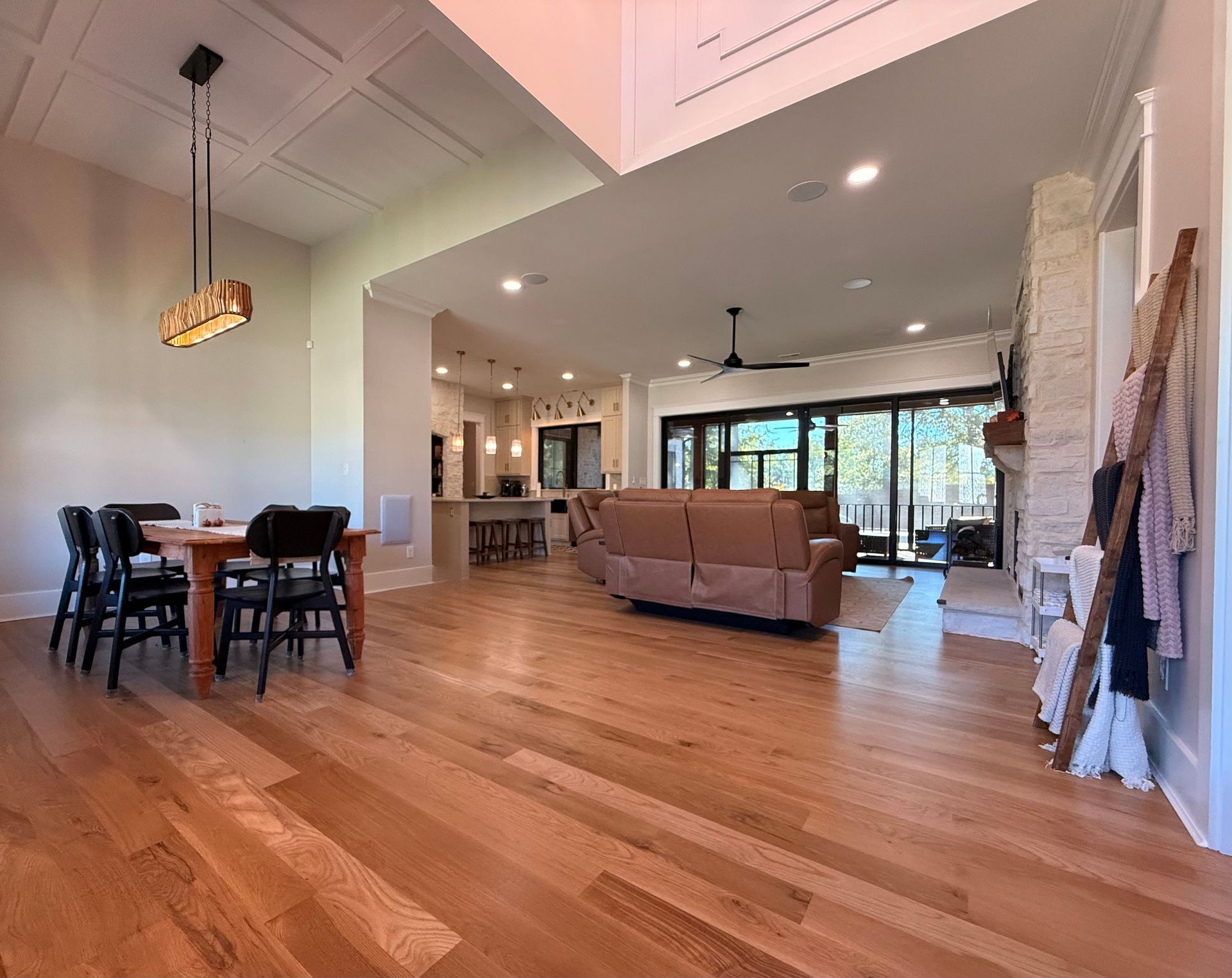 Spacious open-plan living and dining room with hardwood floors, beige sofa, and large windows overlooking greenery