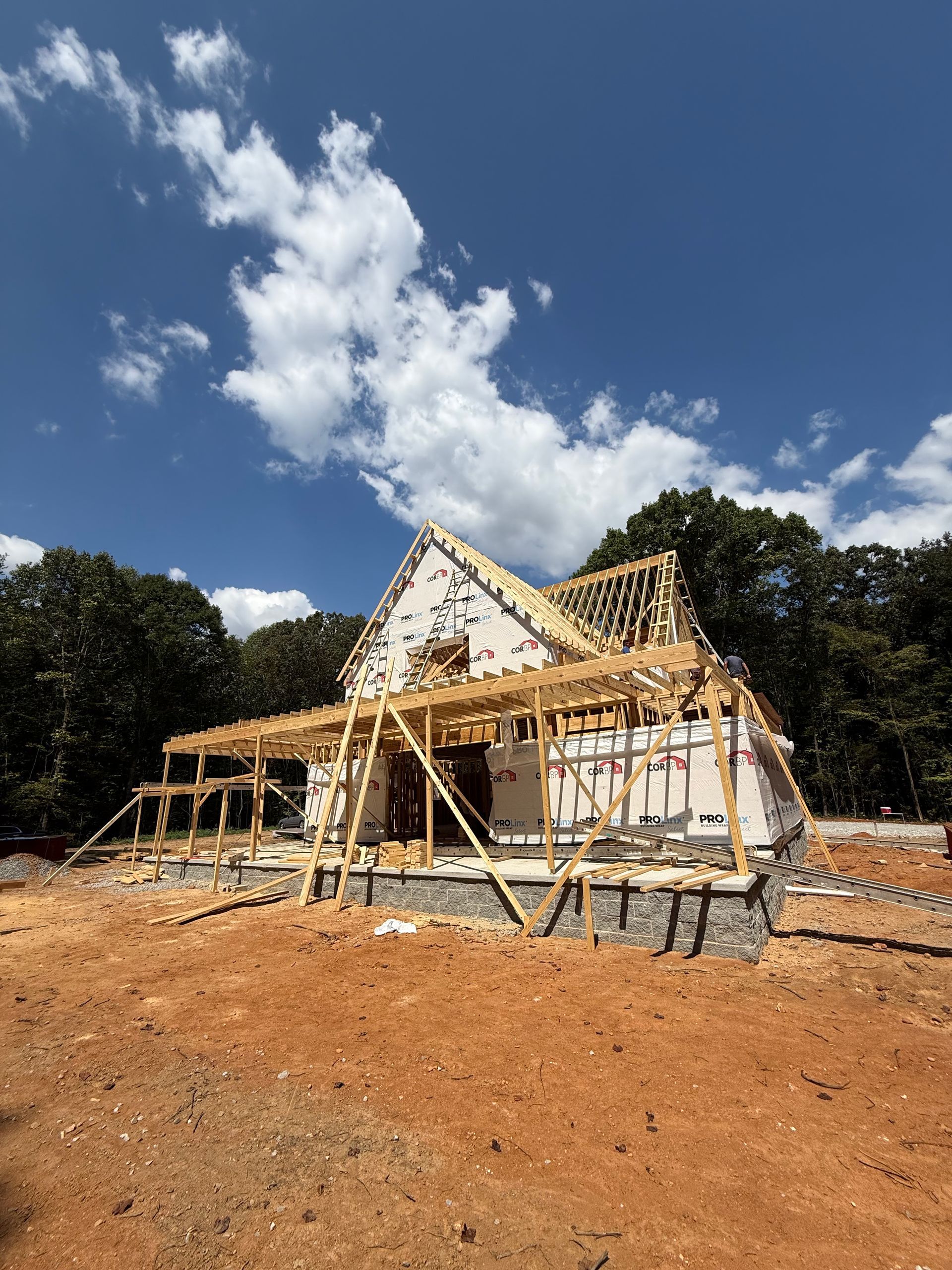 Partially built house with wooden scaffolding under a blue sky on a dirt lot