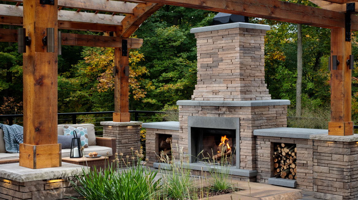 A brick fireplace under a wooden pergola in a backyard.