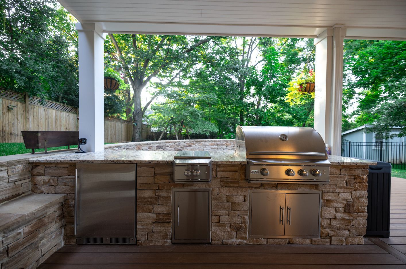 An outdoor kitchen with a grill and a refrigerator under a covered patio.
