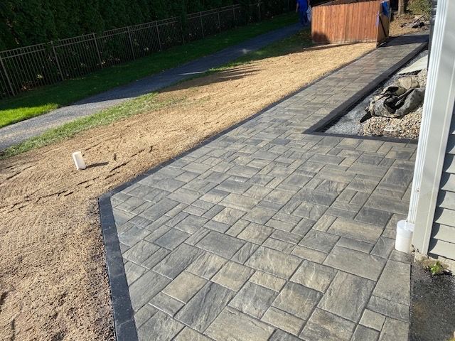 A brick walkway leading to a house with a fence in the background.