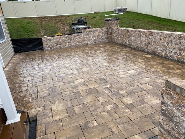 A brick patio with a stone wall in the backyard of a house.