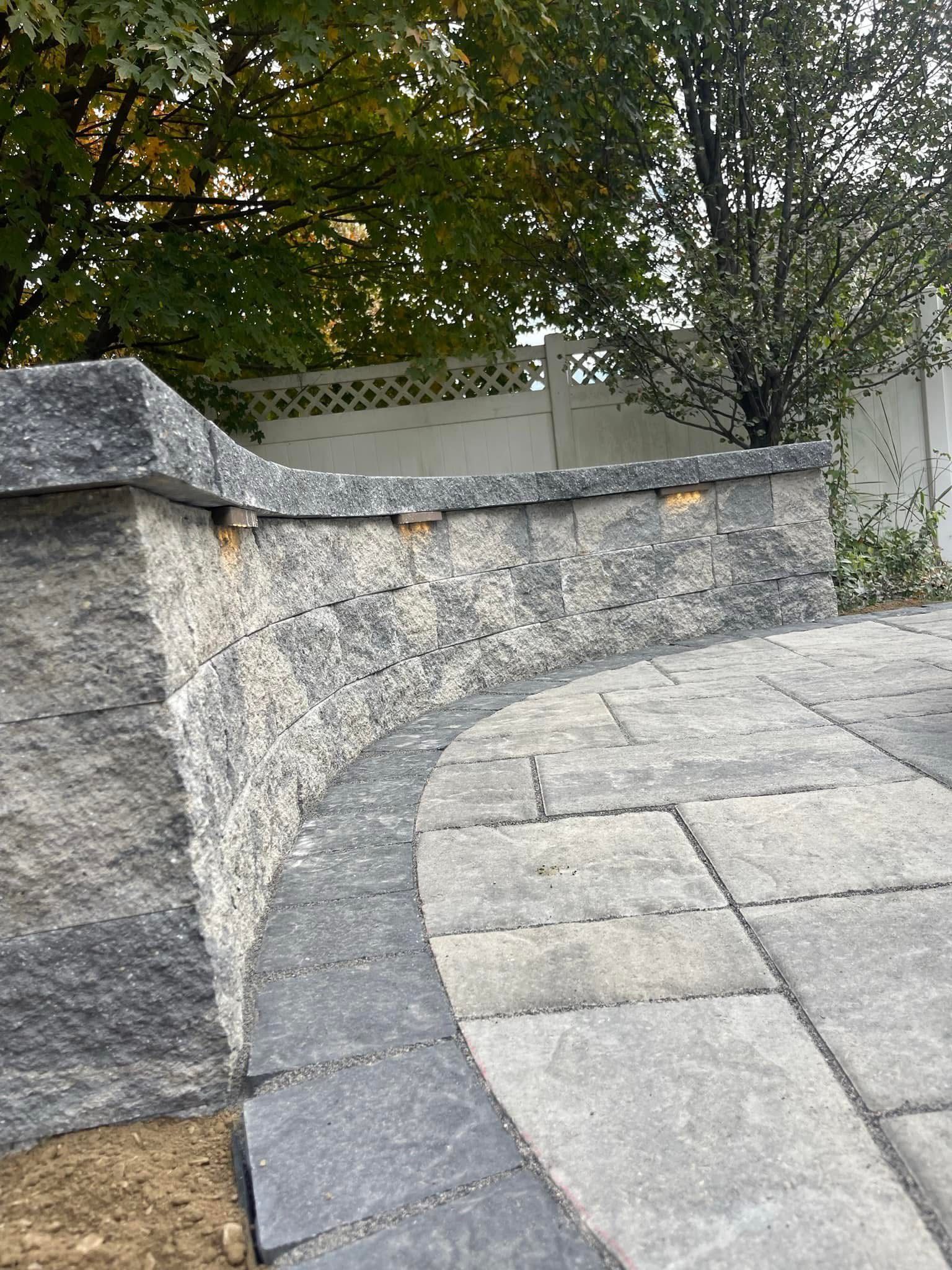 A stone wall with a patio in front of it and trees in the background.