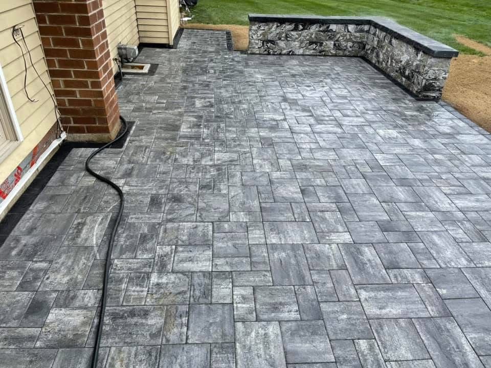A brick patio with a stone wall and a brick chimney in front of a house.