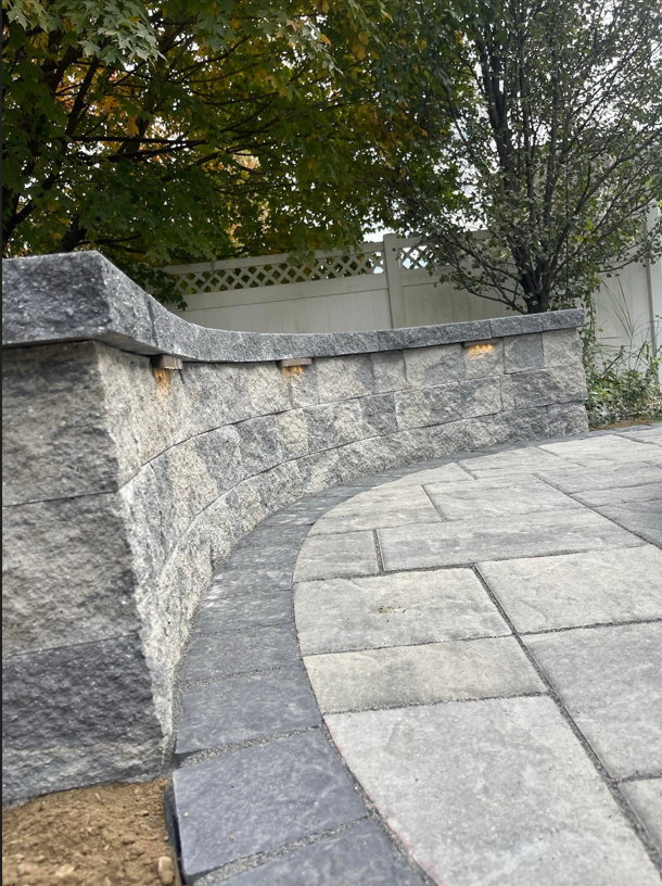 A stone wall surrounds a patio with trees in the background.