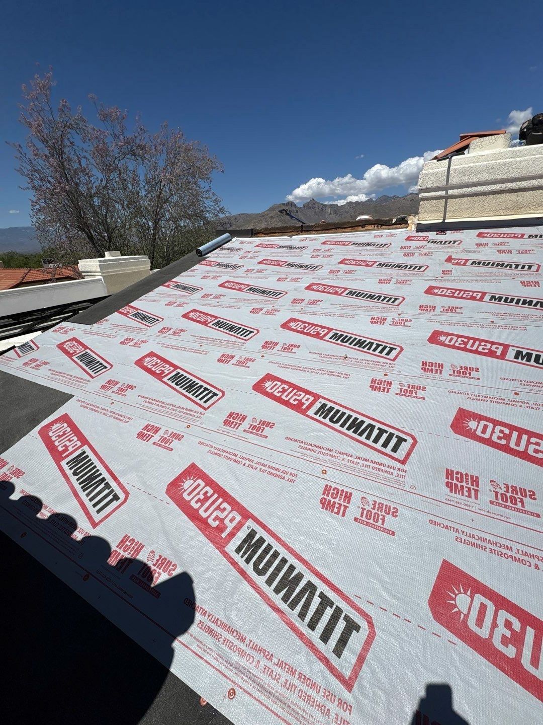 Roof underlayment being installed on a sloped roof under a clear blue sky