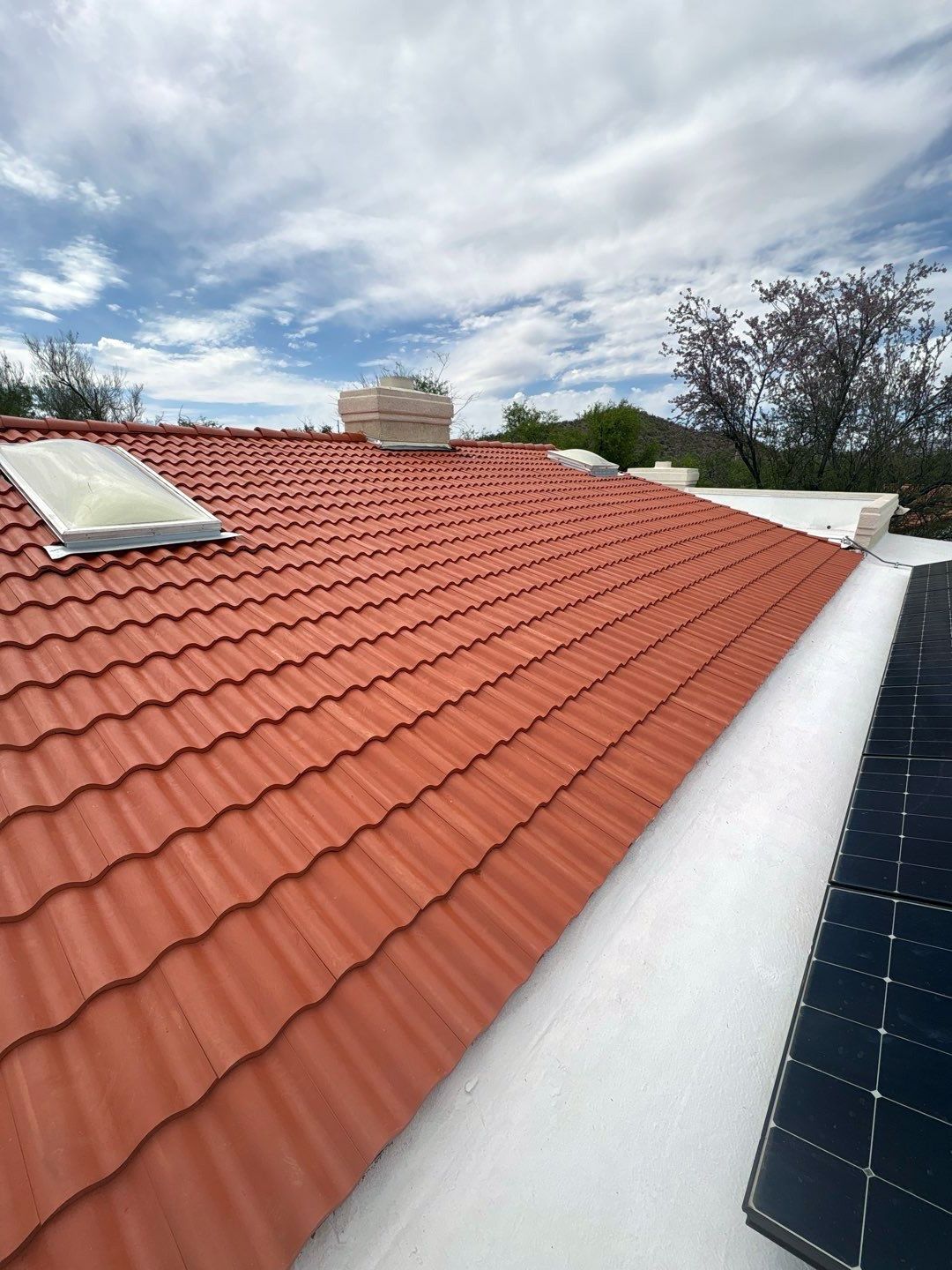 Red tiled rooftop with skylights and solar panels under a cloudy sky