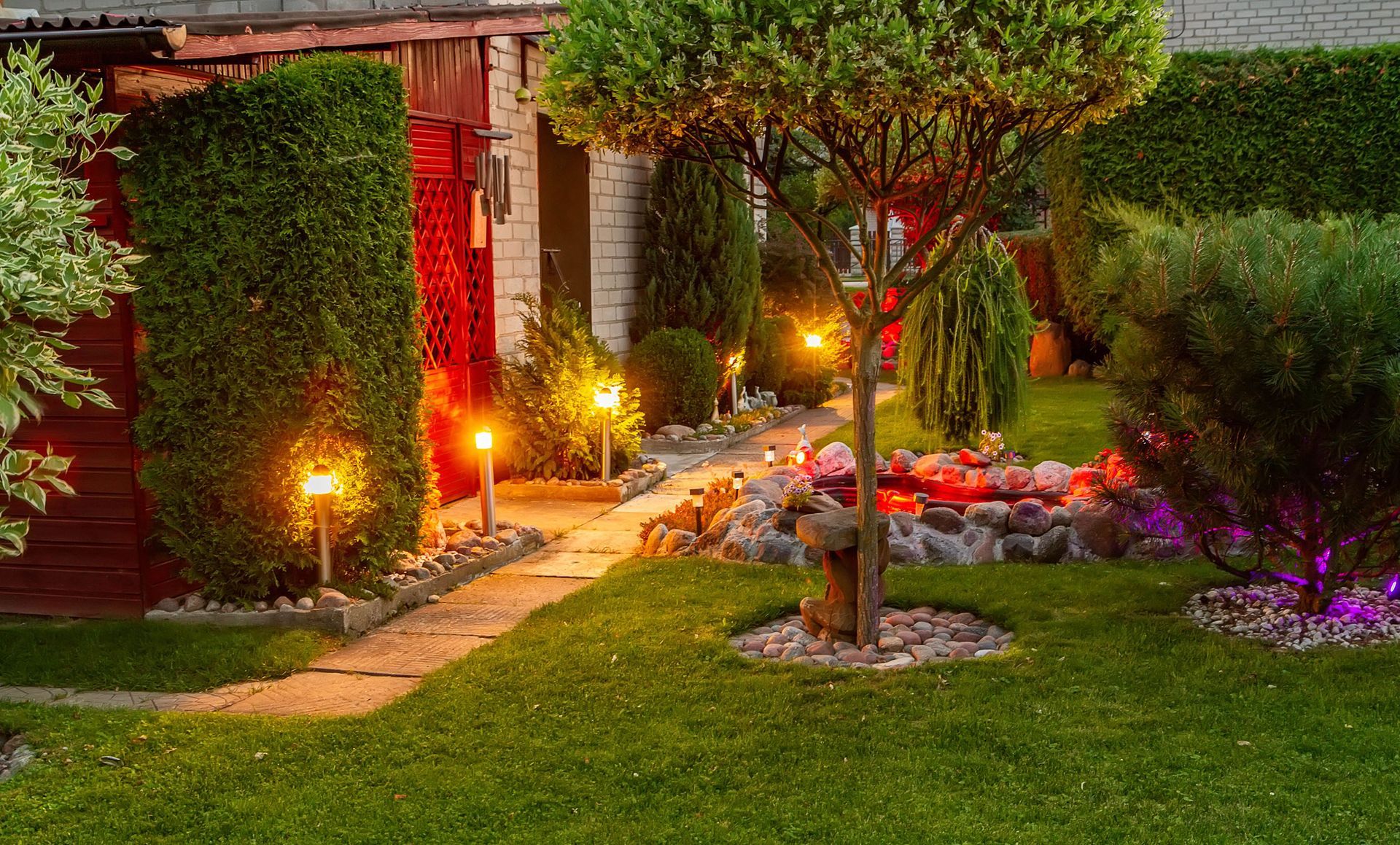 A lush green garden with a path leading to a house at night.