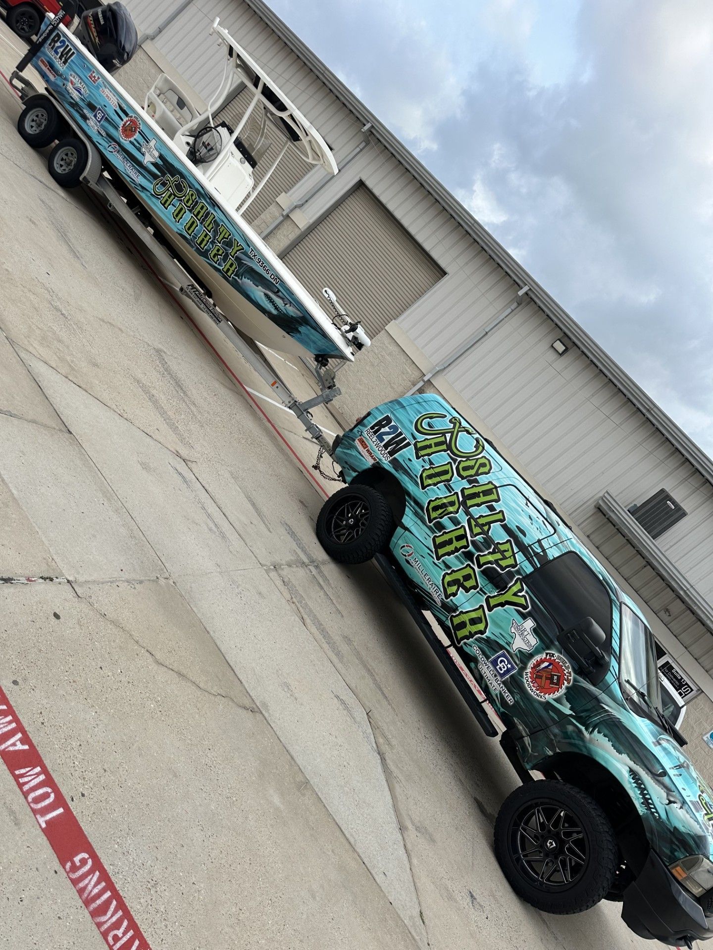 Truck and boat with matching blue and green graphics parked outside a building.